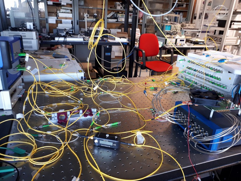 データセンター向け「光スイッチング」の典型的な実験テーブル。 黄色のワイヤーはすべてグラスファイバーでできており、光フィルター（右上）を高度な電子マイクロコンピュータに接続している。